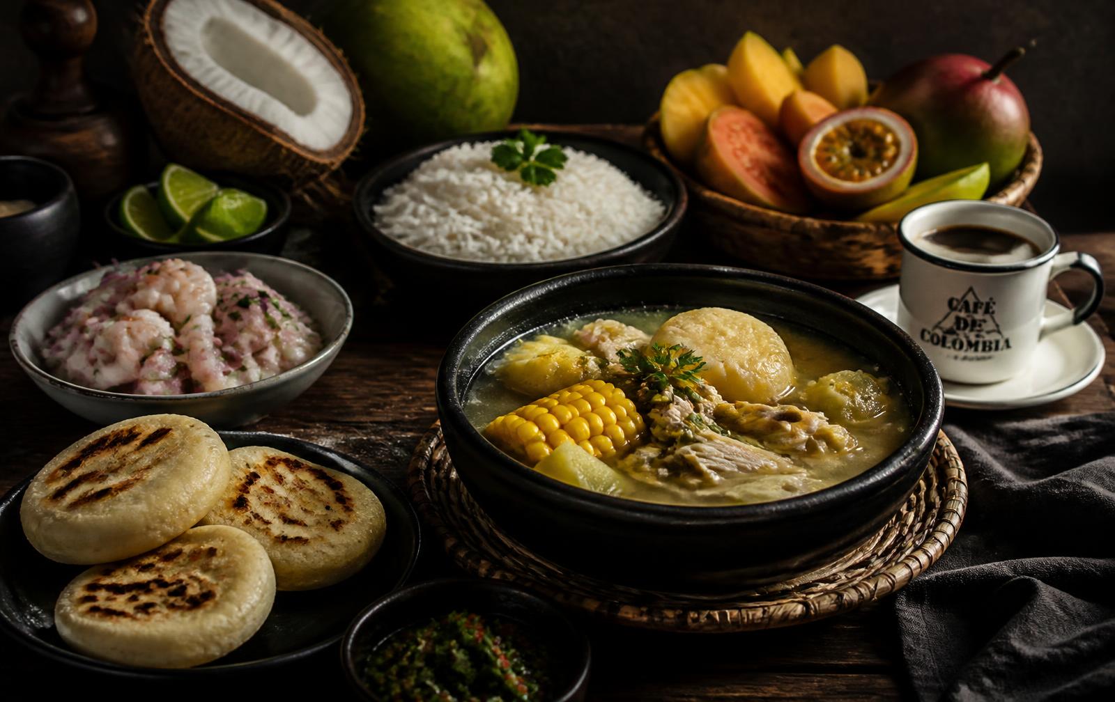 Mesa com pratos colombianos: ajiaco, arepas, ceviche, arroz de coco, frutas tropicais e café